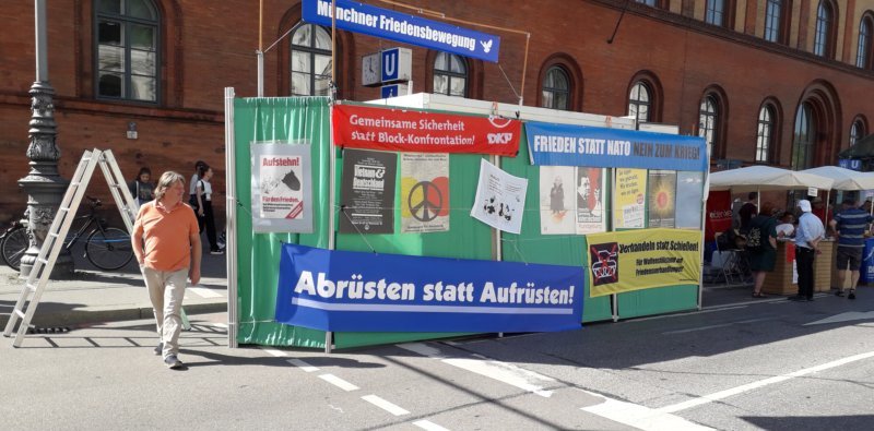 Verkleideter Anhänger mit Ausstellung von Plakaten + Transparenten, ganz oben extra Spruchband Friedensbewegung München mit Taube